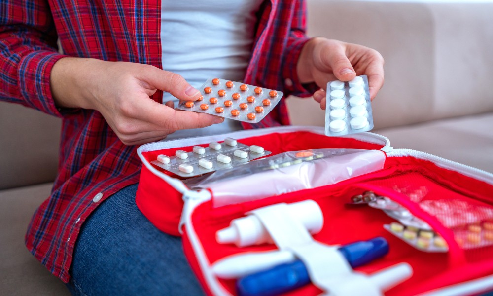 A woman sitting on the couch with an open first aid kit in her lap. She is going though its contents to see what's there.