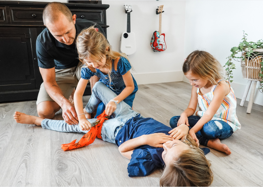 kids simulating a make shift tourniquet on someone's leg using the multi tool triangular bandage and a stick