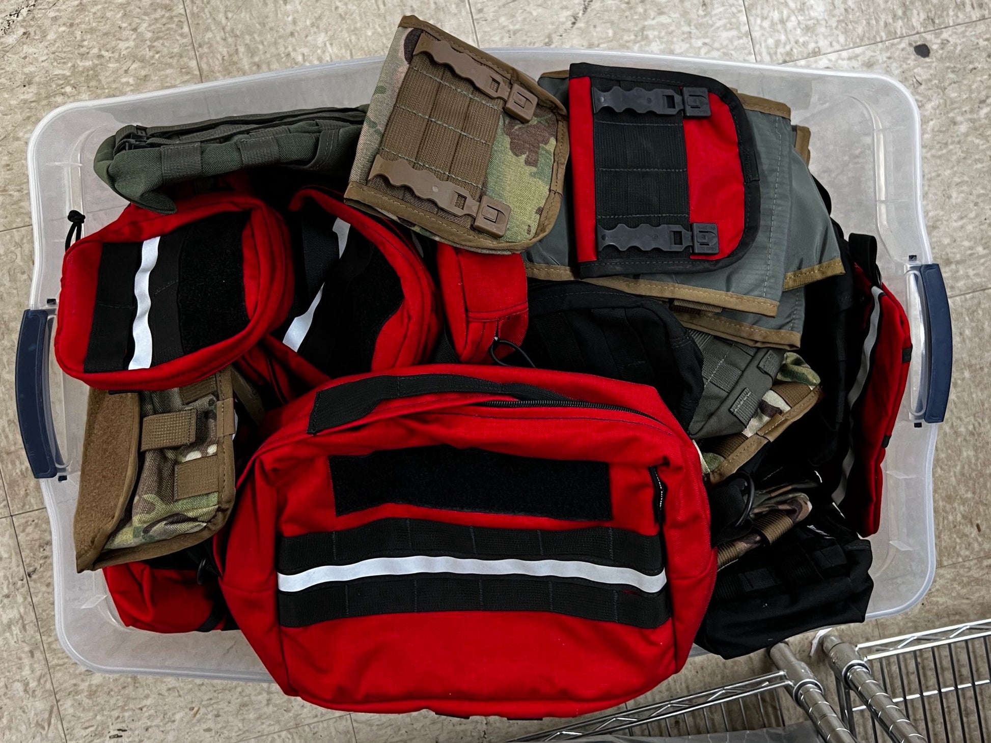 Refuge Medical Grab Bag - A collection of various tactical bags in a transparent plastic storage container, featuring different colors and designs